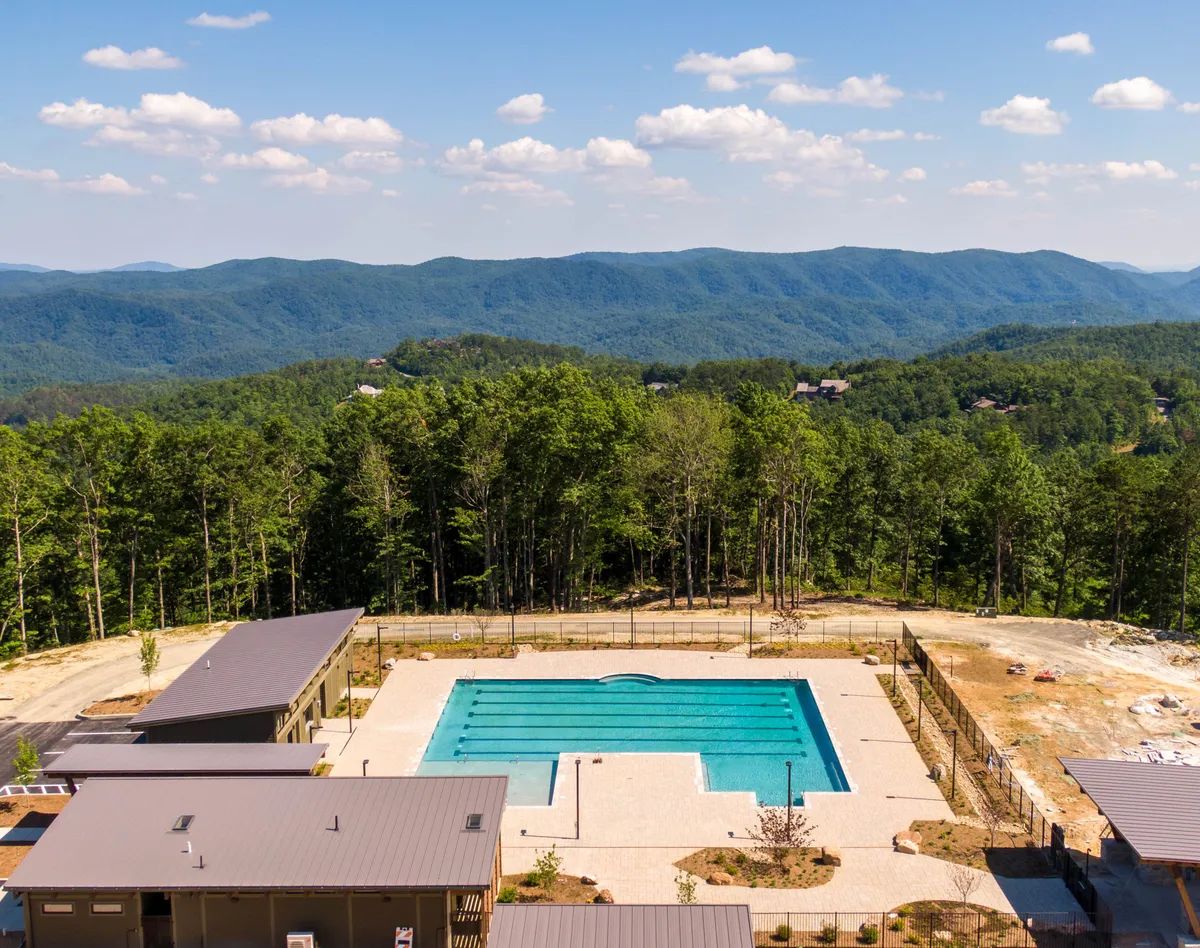 This image features a sparkling outdoor swimming pool set against the backdrop of a scenic mountain range and surrounded by lush trees and modern buildings. The layout showcases ample poolside space for sunbathing and outdoor gatherings, capturing the relaxing, resort-style experience described in the section.