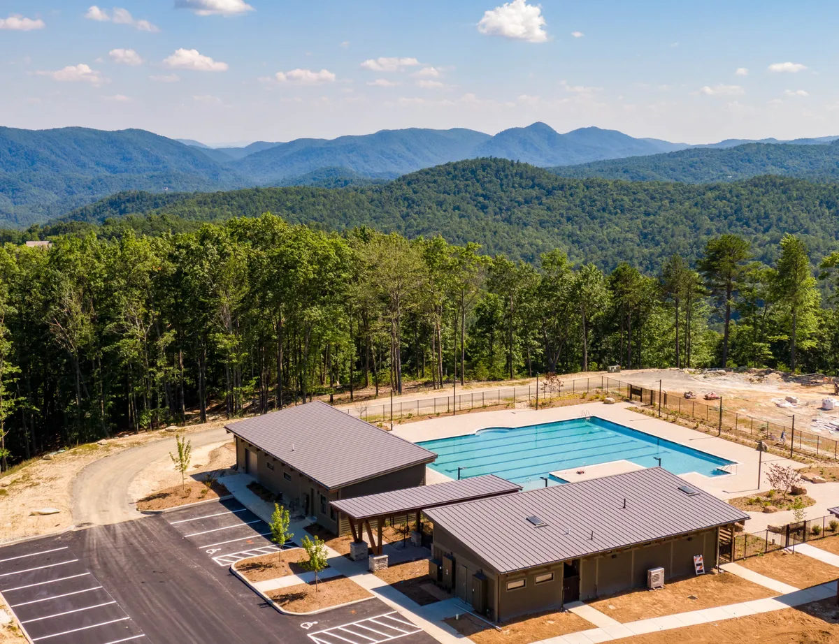 The exterior shot features a swimming pool with mountain views, a clubhouse, and ample space for sunbathing and outdoor gatherings. The setting is perfect for both daytime activities and evening relaxation, capturing the community vibe.