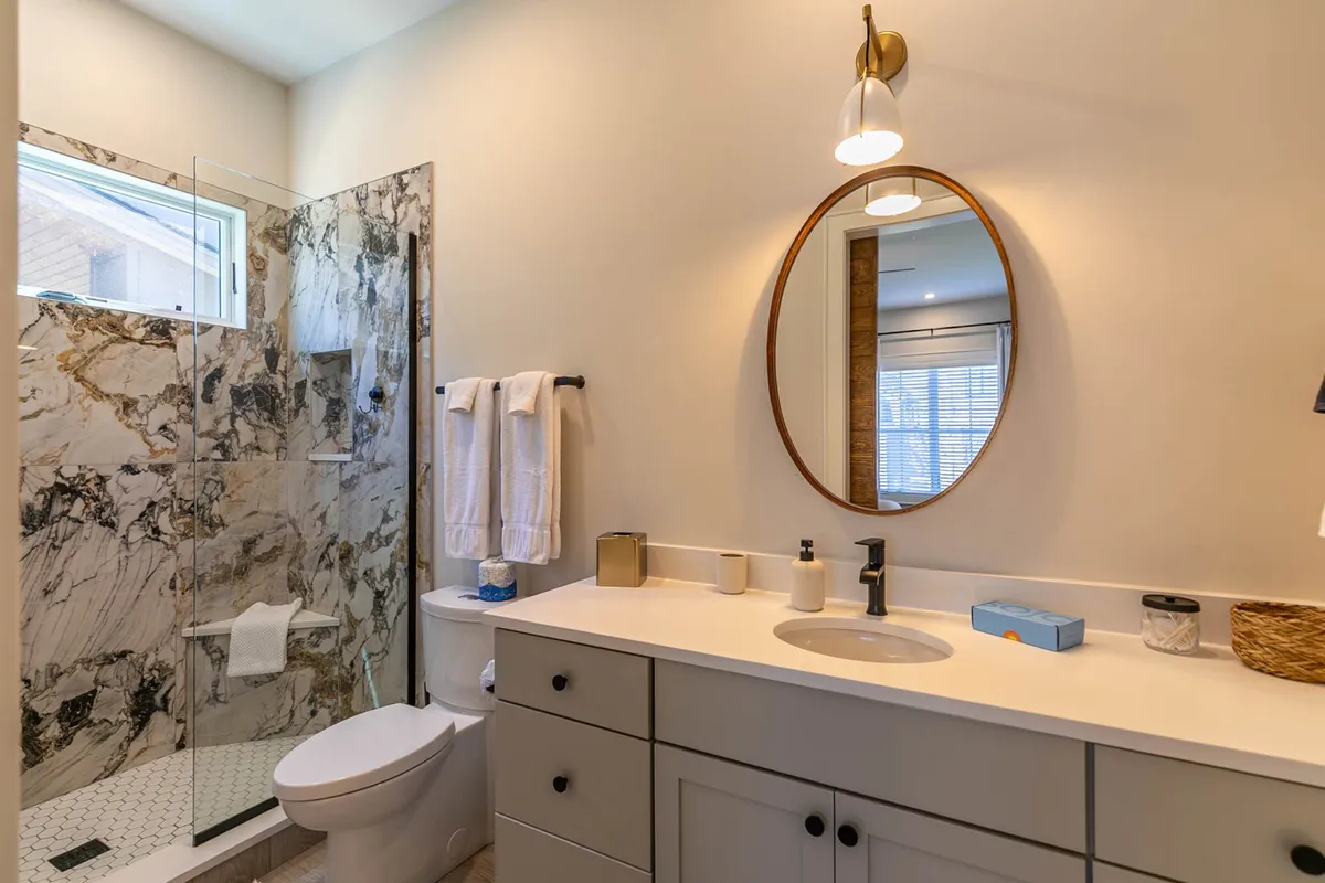A luxurious bathroom with a sleek glass shower enclosure, marble walls, a round mirror, and a modern vanity with a stylish sink. The space feels bright and elegant, designed for self-care and relaxation after a day of adventure.