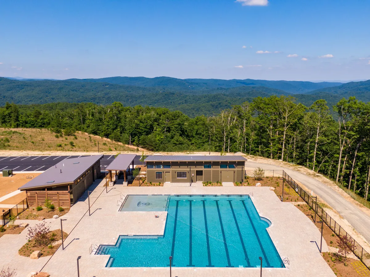 A vibrant view of a swimming pool framed by mountain vistas, landscaped areas, and a visible community building in the background. The setting is lively, hinting at social activities, poolside barbecues, and community events, complementing the festive, communal atmosphere described in the section content.