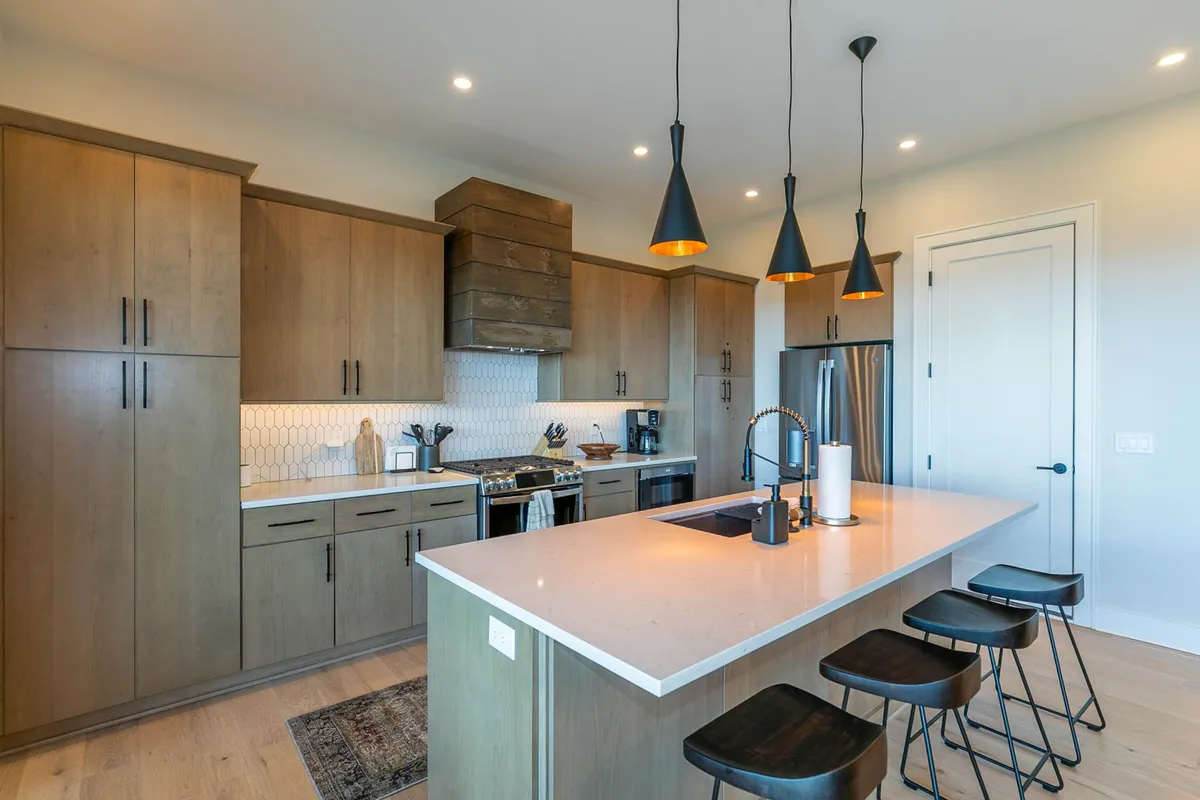 A modern, inviting kitchen with a large island topped by pendant lights, stainless steel appliances, and warm wood cabinetry. The arrangement is ideal for cooking, casual dining, and entertaining guests, emphasizing both functionality and comfort.