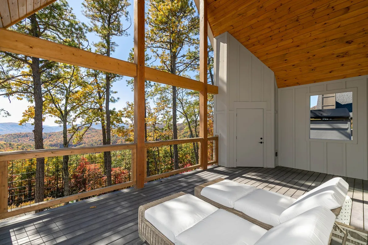 A comfortable outdoor seating area with lounge chairs and a small table, set against an expansive view of the mountains and surrounded by trees with autumn foliage. Natural light filters through the branches, creating a tranquil, inviting spot for relaxation or intimate gatherings under the stars.