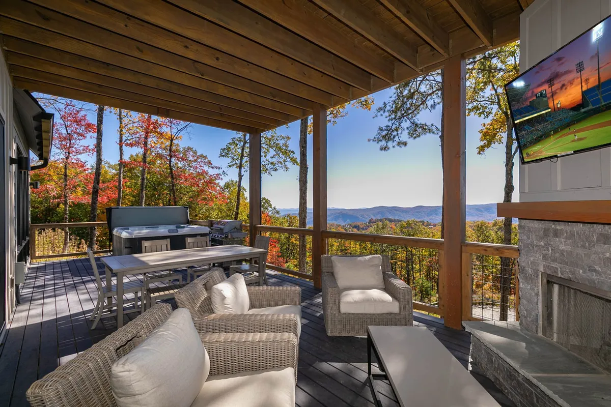 An exterior view of a spacious patio with a seating area, outdoor television, grill station, and panoramic mountain scenery. The scene is set for outdoor dining, socializing, or simply enjoying nature together.
