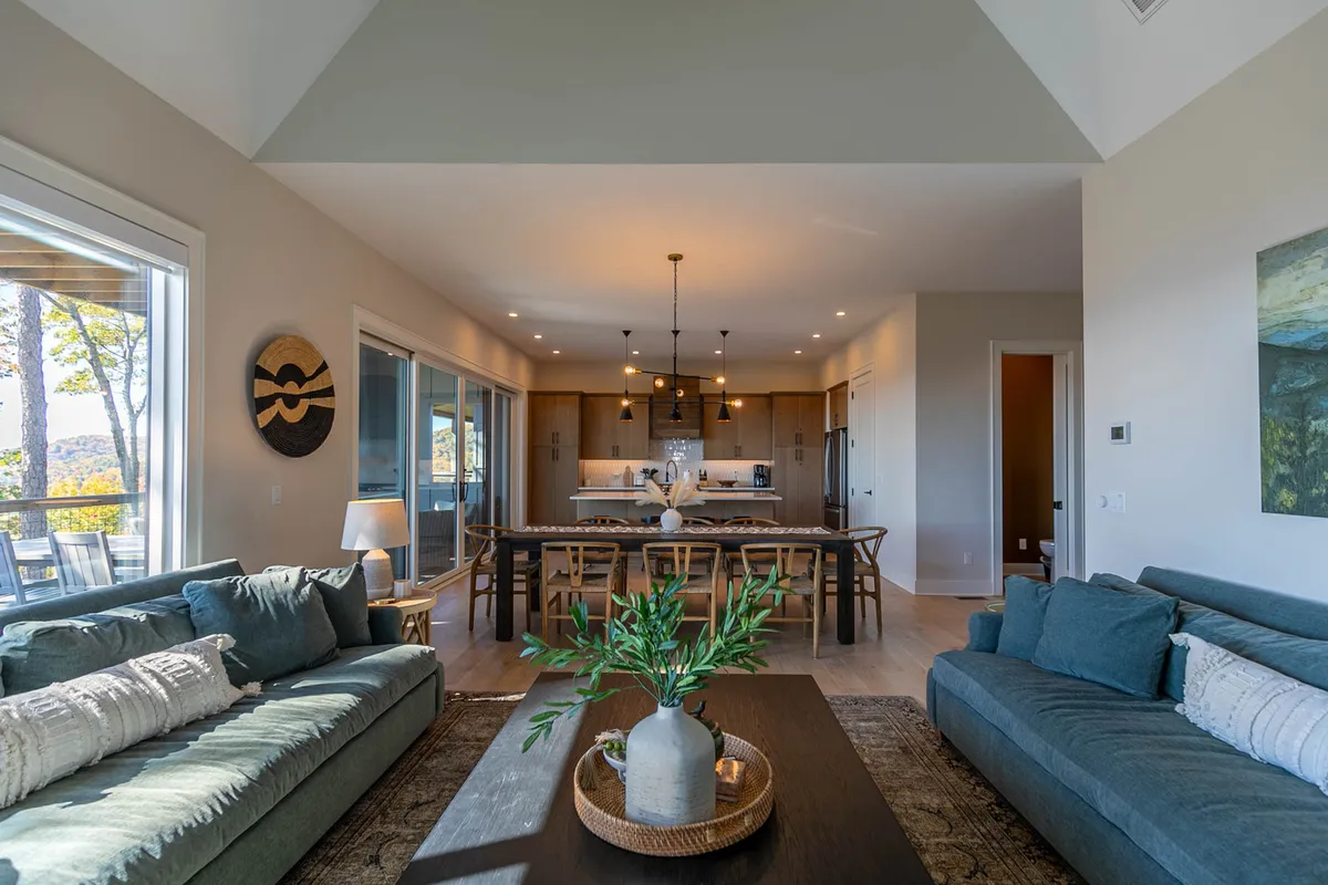 An elegant, open-concept space merges a spacious dining area with a modern kitchen and comfortable sofas. A large dining table is set for family meals, and sunlight streams through expansive windows. The room’s seamless flow makes it ideal for hosting group meals and celebrations.